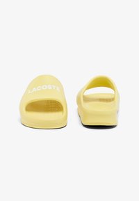 Des sandales jaunes à enfiler en caoutchouc ; dotées d'un design ouvert à l'avant et d'un logo en relief sur le devant. Semelle intérieure texturée pour une meilleure adhérence.