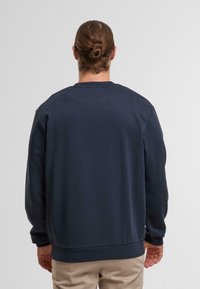 Sweatshirt bleu marine avec un col rond, des poignets et un ourlet côtelés, et une texture lisse, présentant une coupe décontractée et sans logos visibles.
