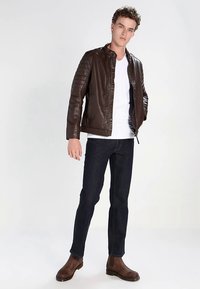 Brun læderjakke med quiltede skulderdetaljer og lynlås. Bruges over en hvid skjorte, kombineret med mørke jeans og brune ankelstøvler.