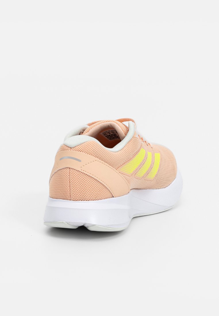 Zapatos deportivos con una parte superior de malla en color durazno claro, tres rayas verticales amarillas y una suela blanca gruesa. Talón reforzado y cuello acolchado.