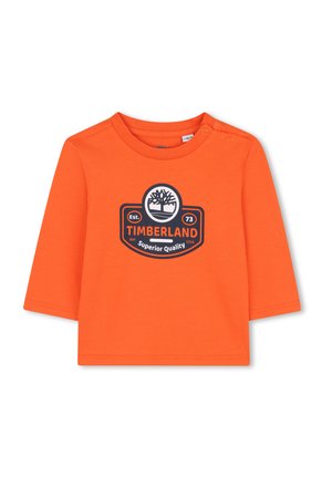 T-shirt à manches longues orange en coton, avec un col rond et des boutons pressions à l'épaule. Détail central avec le logo Timberland en noir.