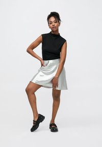 Crni top bez rukava uparen sa srebrnom, sjajnom suknjom skater kroja. Ima glatku teksturu i suptilan sjaj, u kombinaciji s crnom obućom.