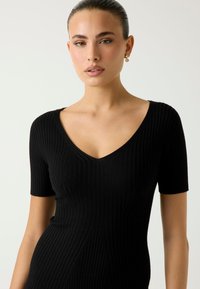 Schwarzes, geripptes Strickkleid mit kurzen Ärmeln und tiefem V-Ausschnitt, das eine figurbetonte Silhouette und strukturierten Stoff betont.