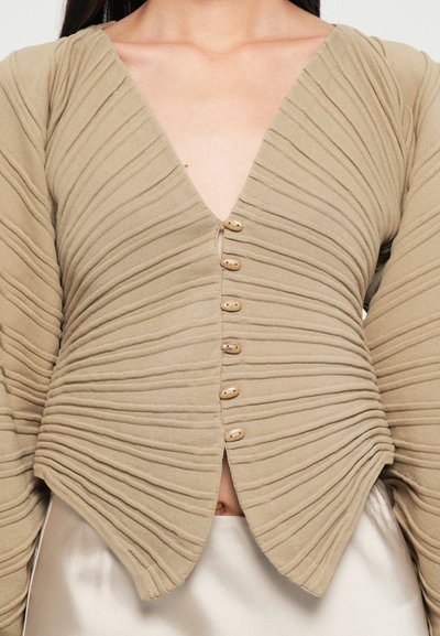Beige ribbed top featuring a deep V-neck, textured fabric with horizontal pleats, and wooden buttons down the front.