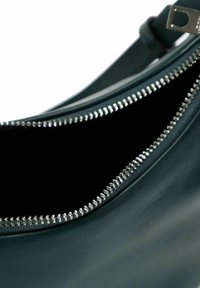 Primer plano de un bolso de cuero verde oscuro abierto con un cierre metálico plateado visible y forro interior negro.
