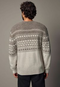 Pull en tricot de couleur gris clair avec des accents marron et des motifs géométriques. Il possède des poignets et un ourlet côtelés, avec une coupe décontractée et une texture douce.