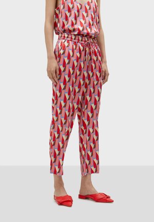 Femme portant un pantalon à motifs géométriques colorés avec taille élastique et cordon de serrage, associé à des ballerines rouges à bout pointu.