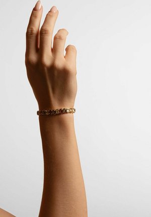 Gold-colored bracelet with rectangular links, featuring a polished surface and slight texture, worn on a hand against a light background.