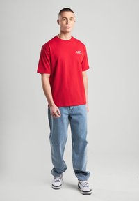 Punainen puuvillapaita, jossa on lyhyet hihat ja pyöreä kaulus, sisältäen valkoisen logon vasemmassa rinnassa. Yhdistetty vaaleansinisiin farkkuihin ja tennareihin.