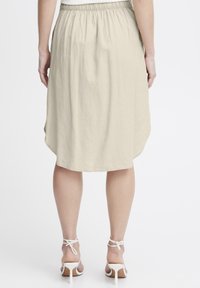 Jupe beige midi avec une taille élastique, arborant une texture douce et un ourlet arrondi. Associée à des sandales à talons hauts blanches avec des lanières.