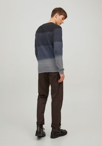 Mænds langærmet sweater i gradient nuancer af grå, med en struktureret overflade. Parret med brune bukser og sorte snørebåndsstøvler.
