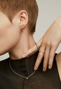 Pendiente de aro de plata y anillos en capas en un modelo, mostrando metal pulido, formas circulares y detalles texturizados contra una blusa oscura.