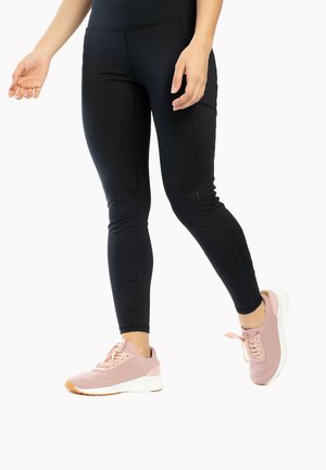 Sorte atletiske leggings med et tætsiddende design, prydet med kontrastsyninger. Sammen med lyserøde mesh sneakers med hvide såler.