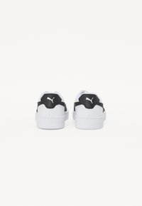 Hvite sneakers med en svart og hvit bakpanel, med en skinnaktig tekstur og en fremtredende logo på hælen. Flat hvit såle.