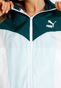 Chaqueta PUMA con un diseño de bloques de color en teal y azul claro, cierre de cremallera, cuello alto y acento de logo en el pecho.