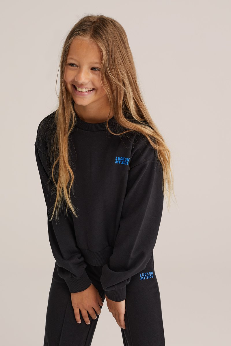 Set de hanorac și pantaloni negri cu manșete striate. Prezintă textul albastru "LUCK ON MY SIDE". Textură moale și croială lejeră.