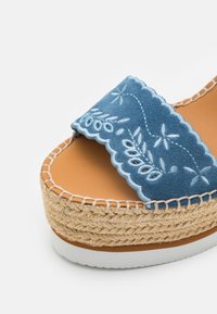Sandale à plateforme en daim bleu avec broderie florale blanche, bride à bord festonné, semelle en jute tissée et semelle extérieure en caoutchouc blanc.