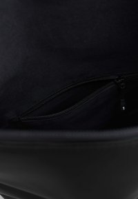 Interior de un bolso de cuero negro que presenta un bolsillo con cremallera y forro de tela. La textura es suave y el diseño es sencillo y funcional.