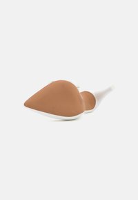 Chaussure à talons hauts blanche avec un design épuré, bout pointu et une semelle en caoutchouc texturé marron. Fini lisse, accents minimalistes.