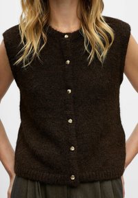 Brauner, gestrickter, ärmelloser Pullover mit rundem Ausschnitt und goldfarbenen Knopfverschlüssen an der Vorderseite. Strukturierter, weicher Stoff.