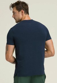 Camiseta de manga corta en azul marino, hecha de algodón suave, con cuello redondo y un diseño de espalda sin costuras con aberturas laterales en el dobladillo.
