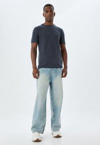 Marineblauwe korte mouwen gebreide trui met ronde hals, gecombineerd met lichtblauwe baggy jeans en witte sneakers. Eenvoudig, casual outfit ontwerp.