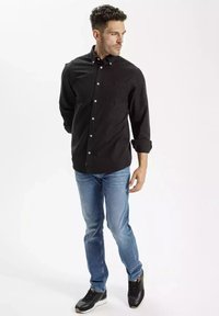 Czarna koszula z długimi rękawami zapinana na guziki, w połączeniu z jasnoniebieskimi dżinsami i czarnymi trampkami. Koszula ma kieszeń i dopasowany krój.