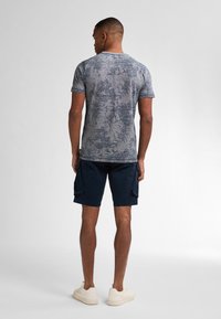 Šedé tričko s krátkým rukávem a texturovaným vzorem, spárované s námořnickými cargo šortkami a krémovými teniskami.