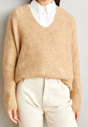 Beige gebreide trui met een V-hals, relaxed fit en geribbelde textuur. Gepaard met lichtgekleurde, rechte broek.