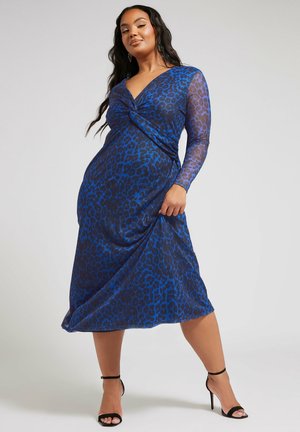 Abito lungo a maniche lunghe in fantasia leopardata teal e nera, con un davanti annodato e gonna fluida, realizzato in un tessuto leggero e leggermente trasparente.