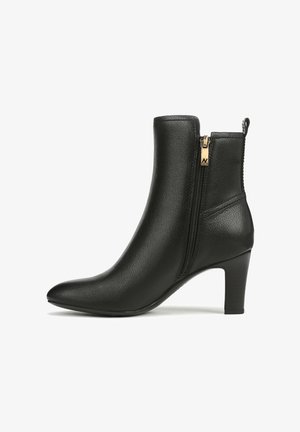 Stivale nero in pelle alla caviglia con punta affilata, cerniera laterale con tirante dorato e tacco medio a blocco su sfondo bianco.