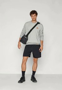 Pilkas ilgomis rankovėmis džemperis, juodos šortai ir juodi sportbačiai. Iš peties kybo mažas juodas krepšys. Sportbačių paviršius yra tekstūruotas.