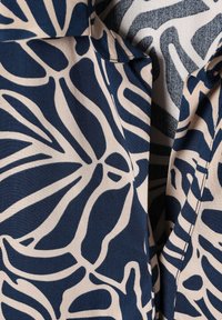 Tissu à motif abstrait de feuilles bleu et beige avec col visible et détails de couture sur un vêtement.