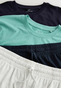 Dwie koszulki z okrągłym dekoltem w kolorach granatowym i morskim oraz spodnie z elastycznym ściągaczem w talii w kolorze granatowym i jasnoszarym, ułożone płasko.