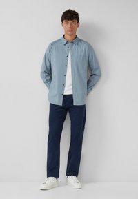 Lichtblauw overhemd met knoopsluiting en een borstzak, gecombineerd met marineblauwe broek en witte sneakers. Glad stof en gestructureerde pasvorm.