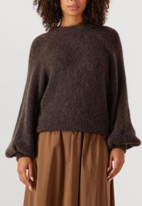 Bruine donzige gebreide trui met een ronde halslijn, brede ballonmouwen en een ontspannen pasvorm, gecombineerd met een bruine geplooide rok.