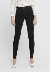 Vaqueros negros ajustados de cintura alta, con trabillas y una textura suave; combinados con una blusa de crochet blanca y tacones blancos.