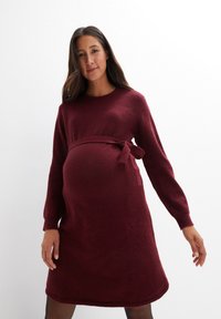 Burgunderfarbendes Strick-Maternity-Kleid mit langen Ärmeln, runder Halslinie und Taillenbindung. Weicher Stoff mit lockerer Passform, knielange Ausführung.