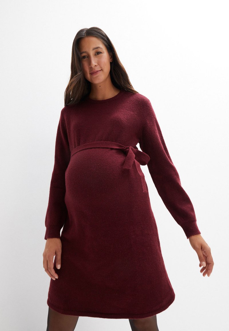 Burgunderfarbendes Strick-Maternity-Kleid mit langen Ärmeln, runder Halslinie und Taillenbindung. Weicher Stoff mit lockerer Passform, knielange Ausführung.