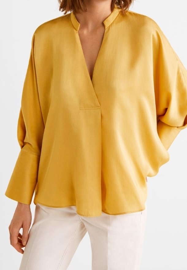Blouse ample jaune moutarde avec larges poignets et fente en V au col, associée à un pantalon écru.