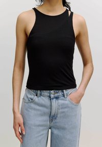 Zwarte geribbelde tanktop met een hoge halslijn en dunne bandjes, gecombineerd met lichtblauwe high-waisted denim jeans met zakken aan de voorkant.