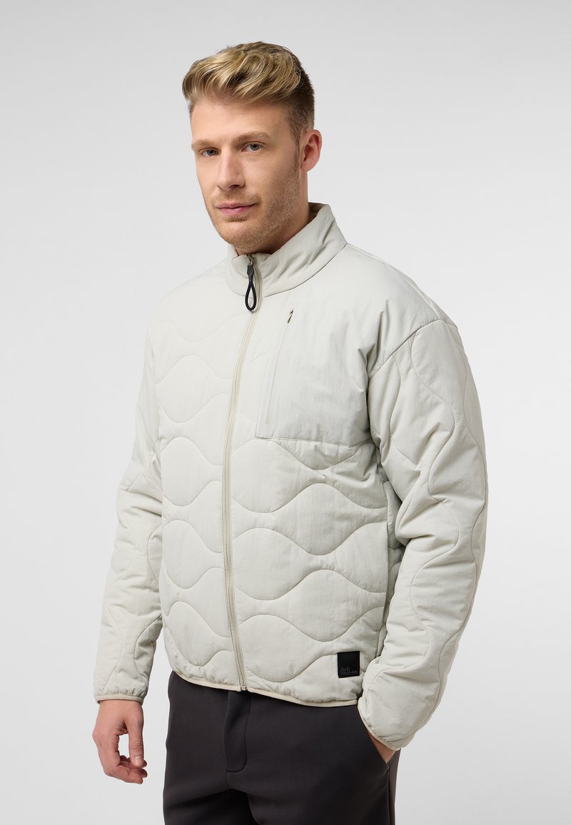 Veste matelassée gris clair avec un col montant, un devant zippé et une poche. Présente un motif en vagues et un petit logo sur l'ourlet.