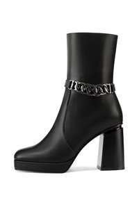 Stivale corto in pelle nera con punta quadrata, tacco a blocco robusto e una catena argentata decorativa attorno alla caviglia. Texture liscia.