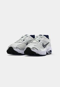 Białe siateczkowe buty sportowe z granatowymi akcentami, fakturowana powierzchnia, wyściełany kołnierz i czarna gumowa podeszwa. Zawierają logo Nike z boku.