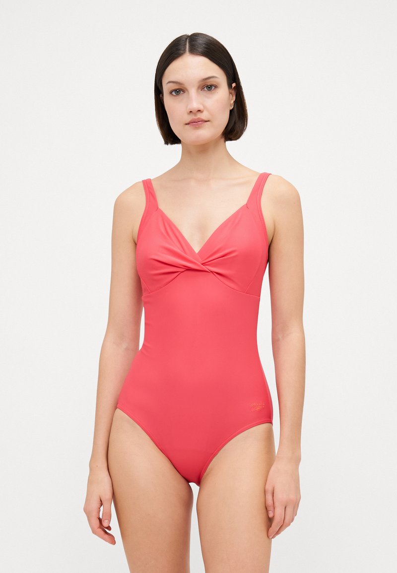 Maillot de bain une pièce rouge avec un design frontal torsadé, des bretelles étroites et une texture lisse et extensible. Présente un logo subtil au niveau de la hanche.