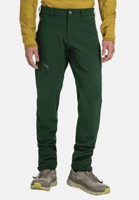 Grüne Outdoor-Hosen aus flexiblem Material mit Reißverschlusstaschen und figurschmeichelndem Design. Getragen mit grauen Wanderschuhen.