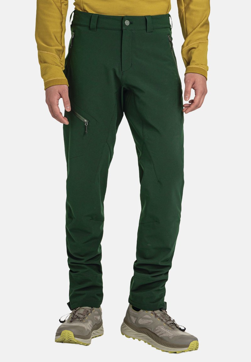 Grüne Outdoor-Hosen aus flexiblem Material mit Reißverschlusstaschen und figurschmeichelndem Design. Getragen mit grauen Wanderschuhen.