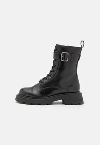Botín de cuero negro hasta el tobillo con puntera redonda, diseño con cordones, correa lateral con hebilla metálica y suela de goma gruesa.