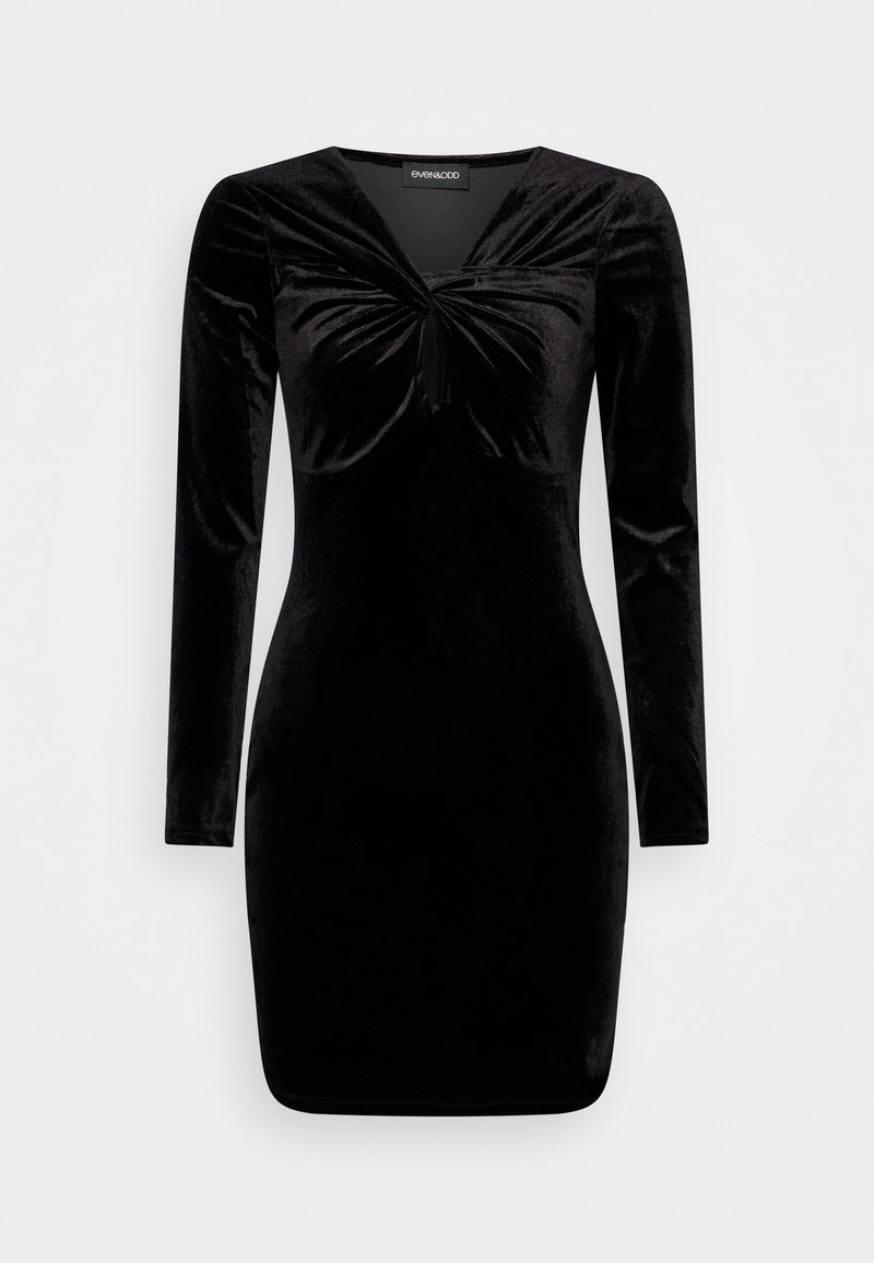 Robe longue en velours noir à manches longues, cintrée, avec un détail noué et une petite ouverture discrète au niveau du buste, longueur au genou.