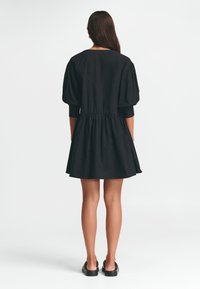 Schwarzes Kleid mit puffärmel, tailliertem Schnitt und weit schwingendem Rock. Hergestellt aus glattem Stoff mit minimalistischer Gestaltung. Keine sichtbaren Muster oder Beschläge.